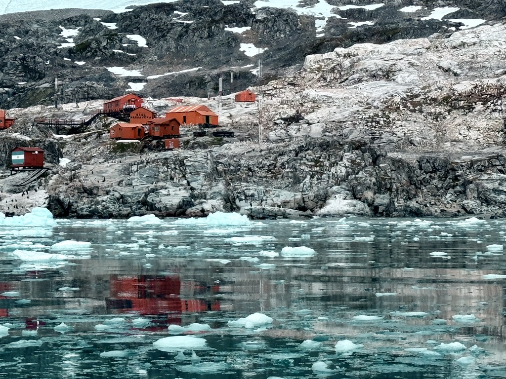 Red buildings on a rocky Antarctic shore reflected in icy water