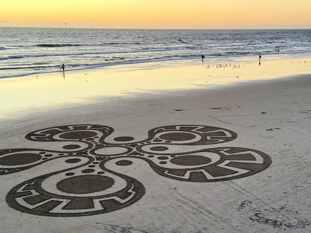 An intricate sand drawing beside the ocean at sunset