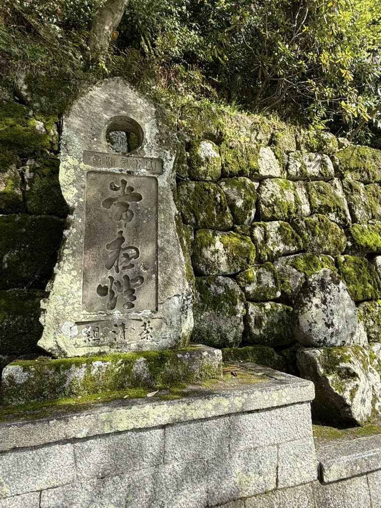 A Japanese stone monument beside a moss-covered wall