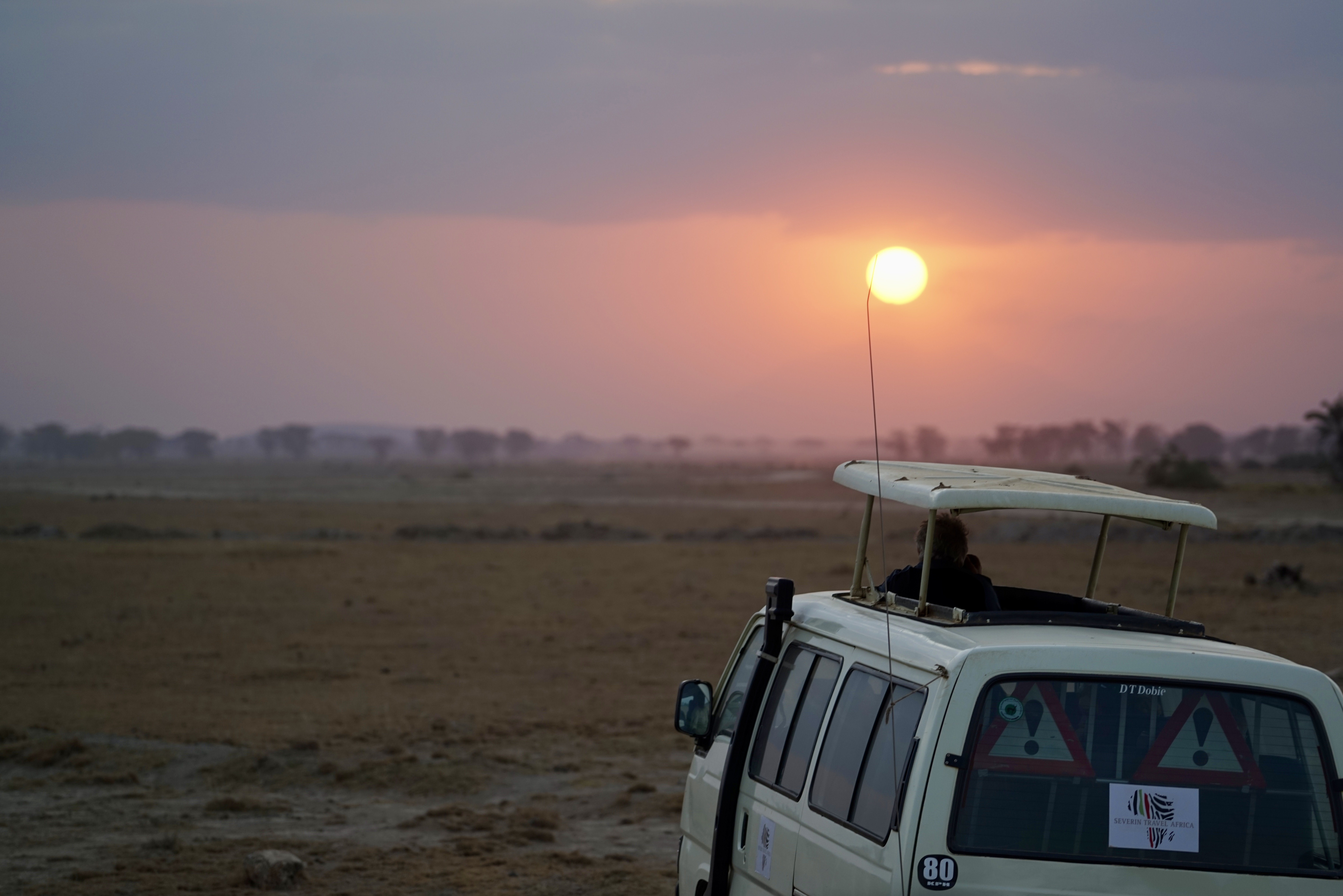 A safari vehicle beneath the setting sun on an open plain