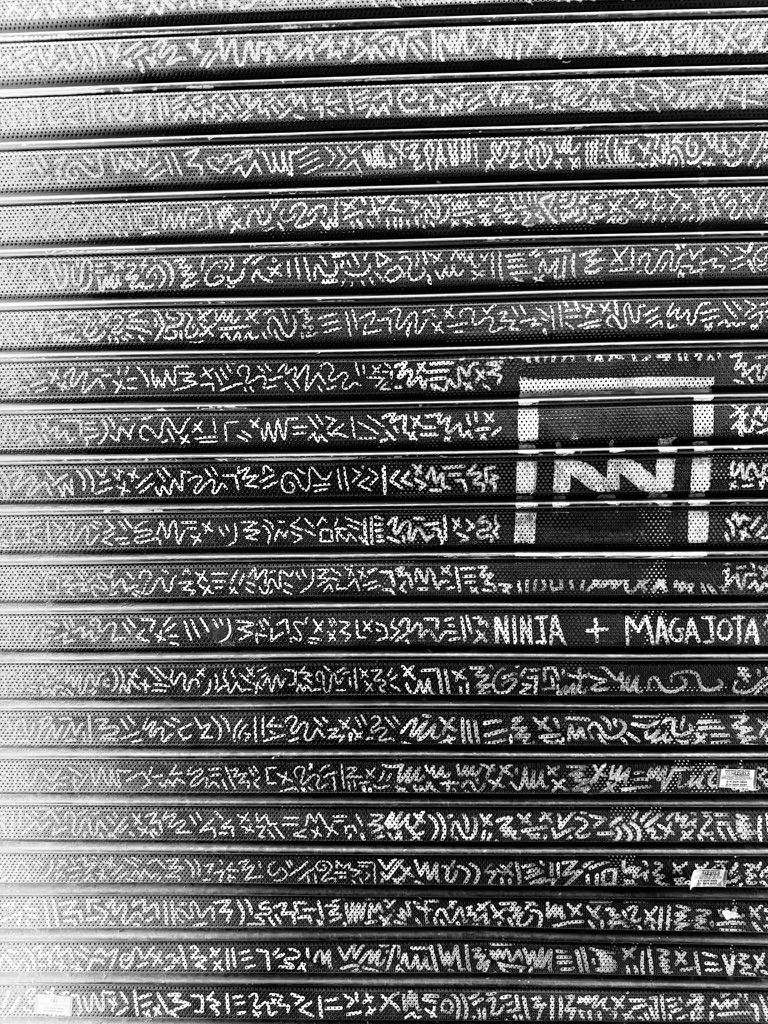 Handwritten markings on a metal shutter in black and white