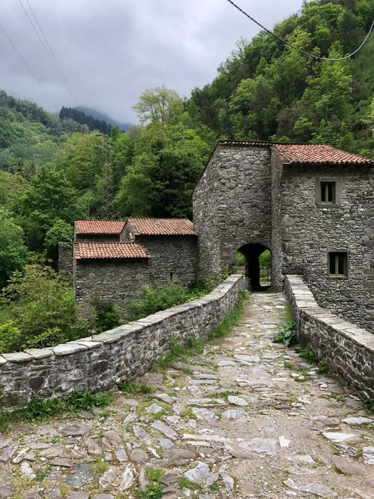 Old stone bridge leading through a building in a green Italian valley